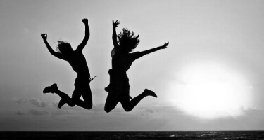 Two ladies jumping in the ear with the hands raised up and legs bend