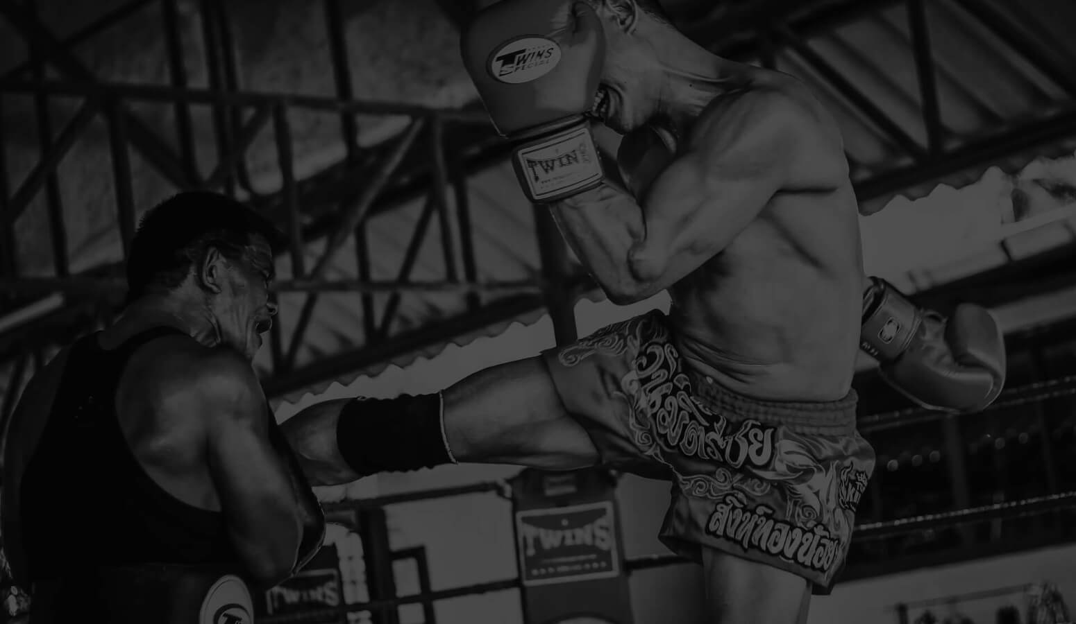 Muay Thai fighter kicking the pad in the ring ,that his trainer is holding for him to practice